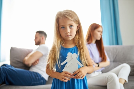 A sad little girl with parents upset at each other in background