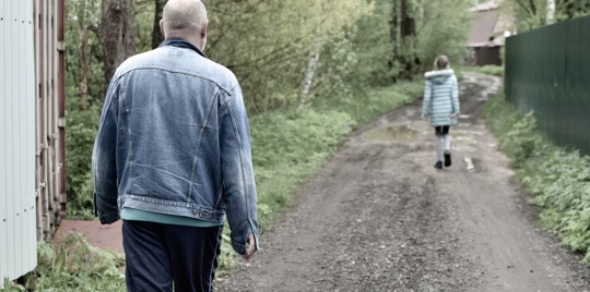 Older man following child at a distance in an alleyway