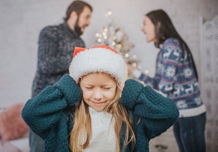 Divorce: Child covering ears with Santa hat as parents fight in the background